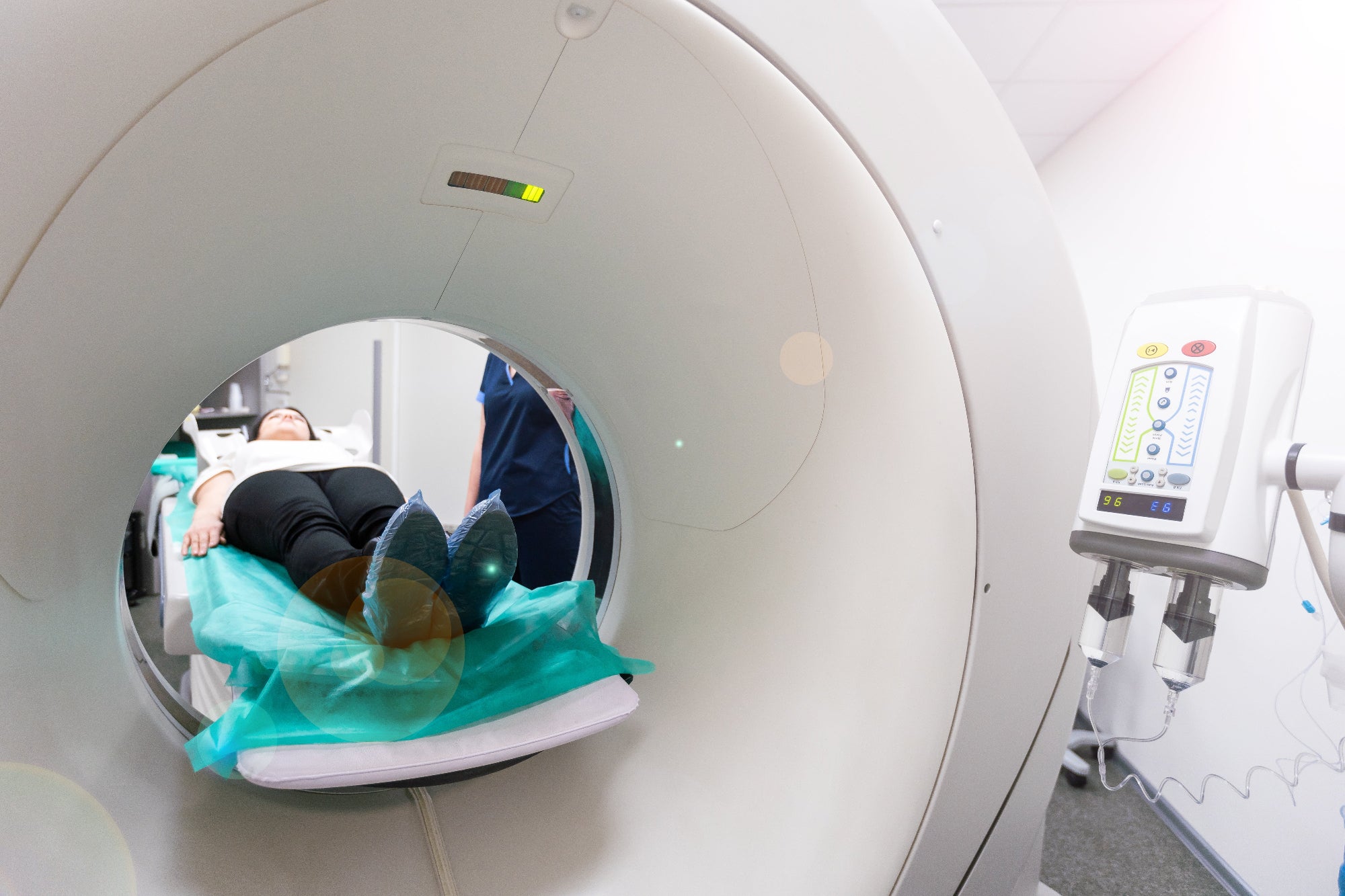 Patient undergoing CT scan with technician and contrast injector in hospital imaging suite
